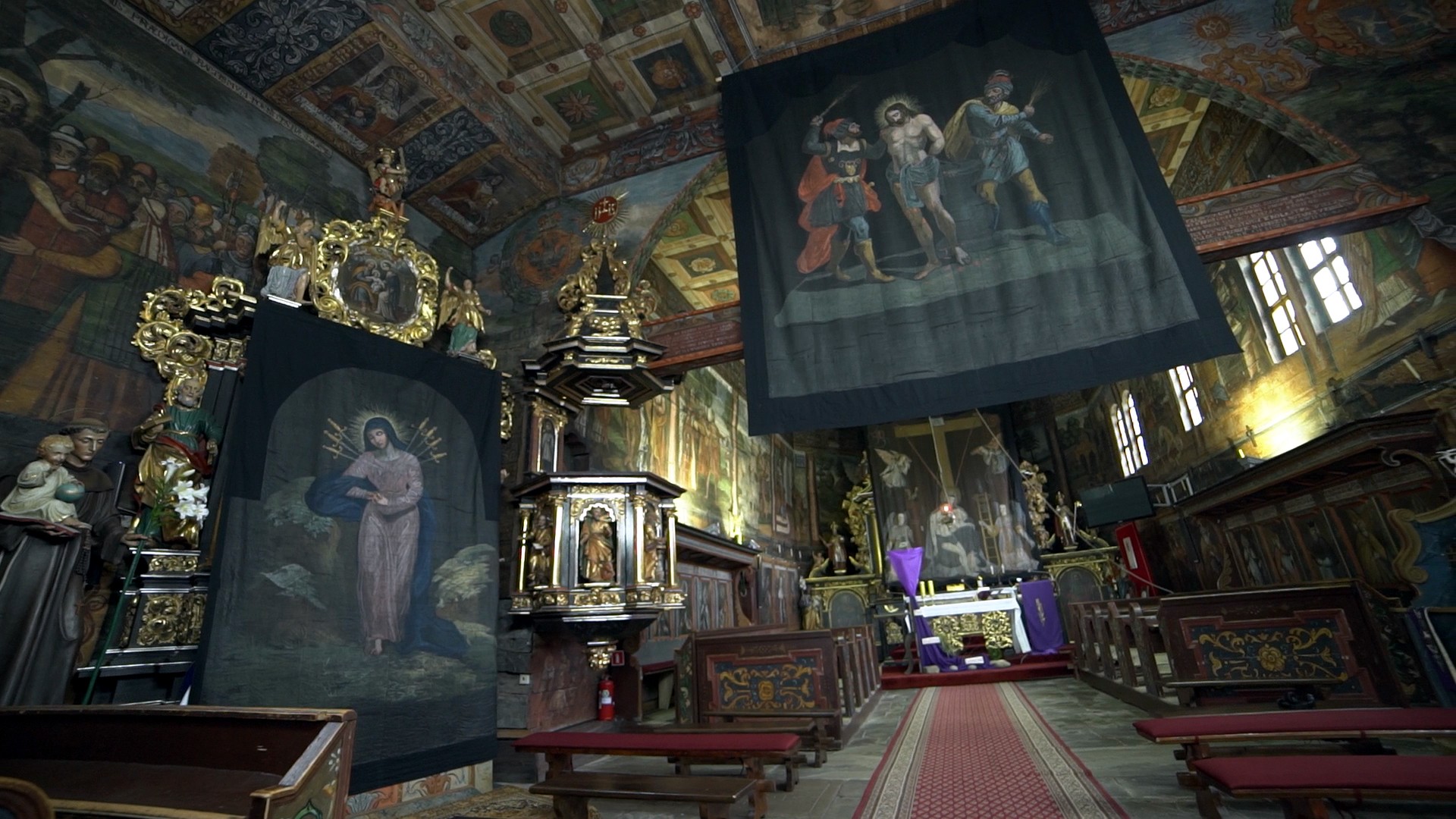 wnętrze kościoła - po lewej płótno z Matką Boską siedmiobolesną, w plecy wbite ma sztylety. W głębi ołtarz. Z sufitu zwisa płótno ze sceną chłosty Jezusa